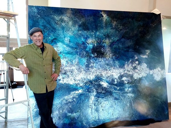 Artist Scott Forrest standing in front of one of his large blue paintings